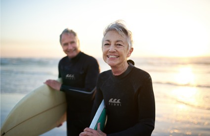 senior couple in wet suits with surf boards
